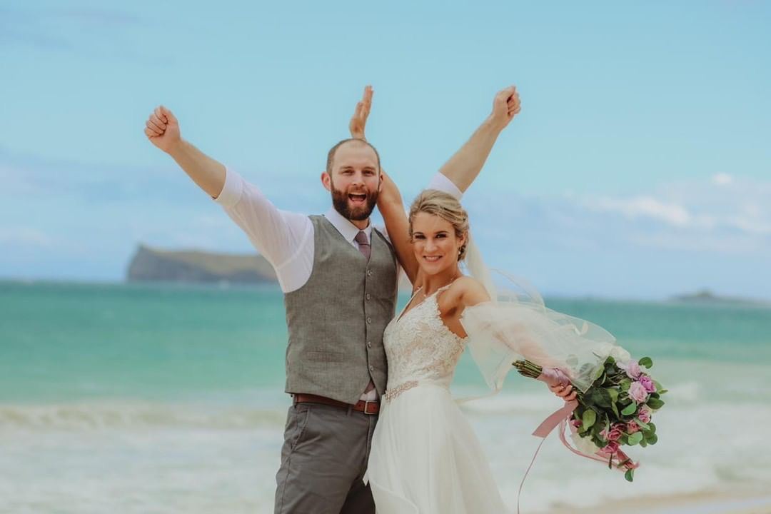 Сouple wearing a white gown and a gray suit on the beach