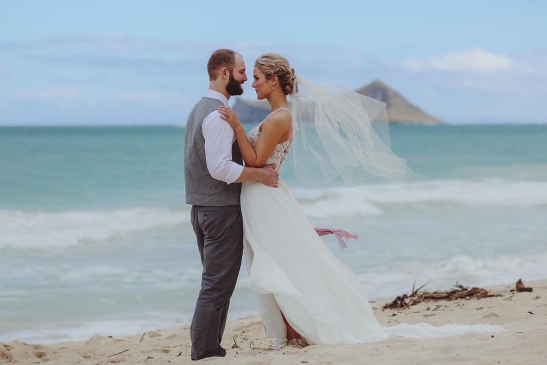 Сouple wearing a white gown and a grey suit on the beach